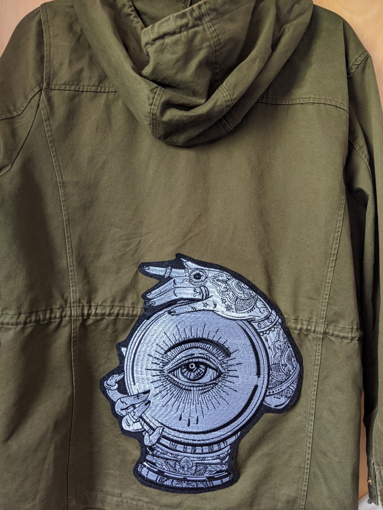 khaki jacket with a black and white crystal-ball-and-hands back patch.