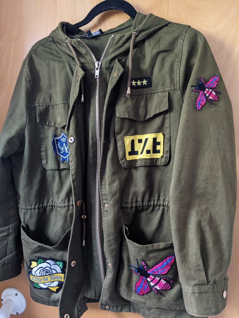 khaki jacket with various patches including Aglionby Academy, Fun Ghoul, Little But Fierce and pink bees.