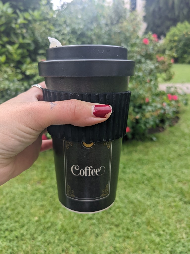 hand holding black travel mug with a tarot design reading 'coffee'