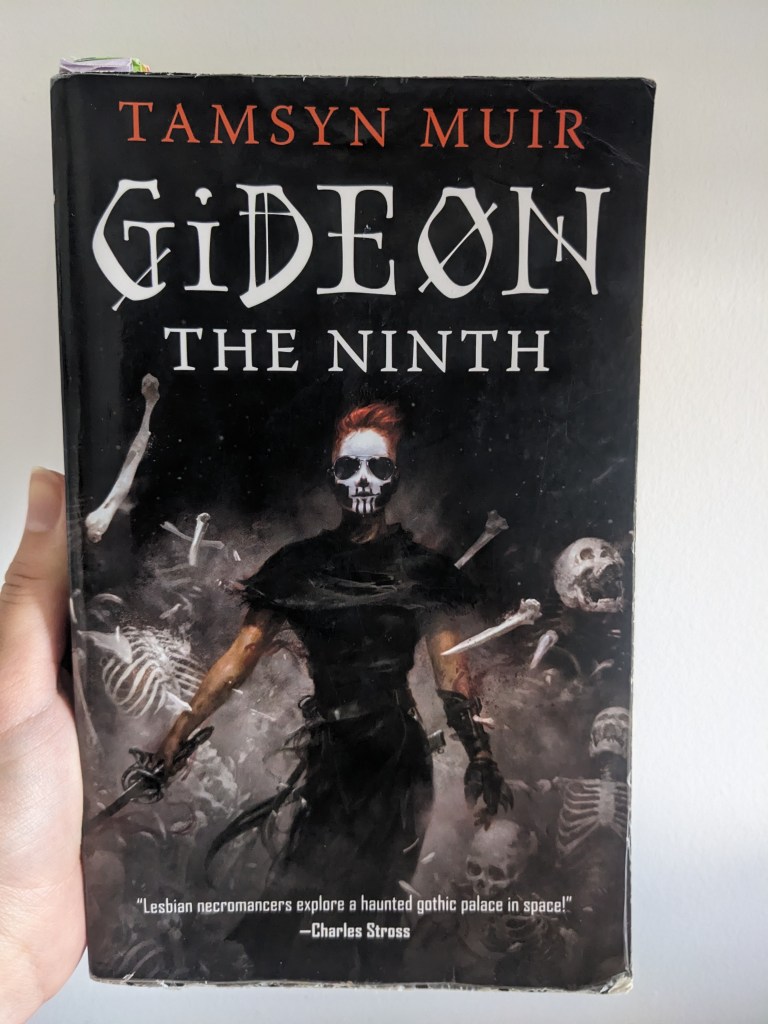 hand holding up a battered paperback of 'Gideon the Ninth' by Tamsyn Muir