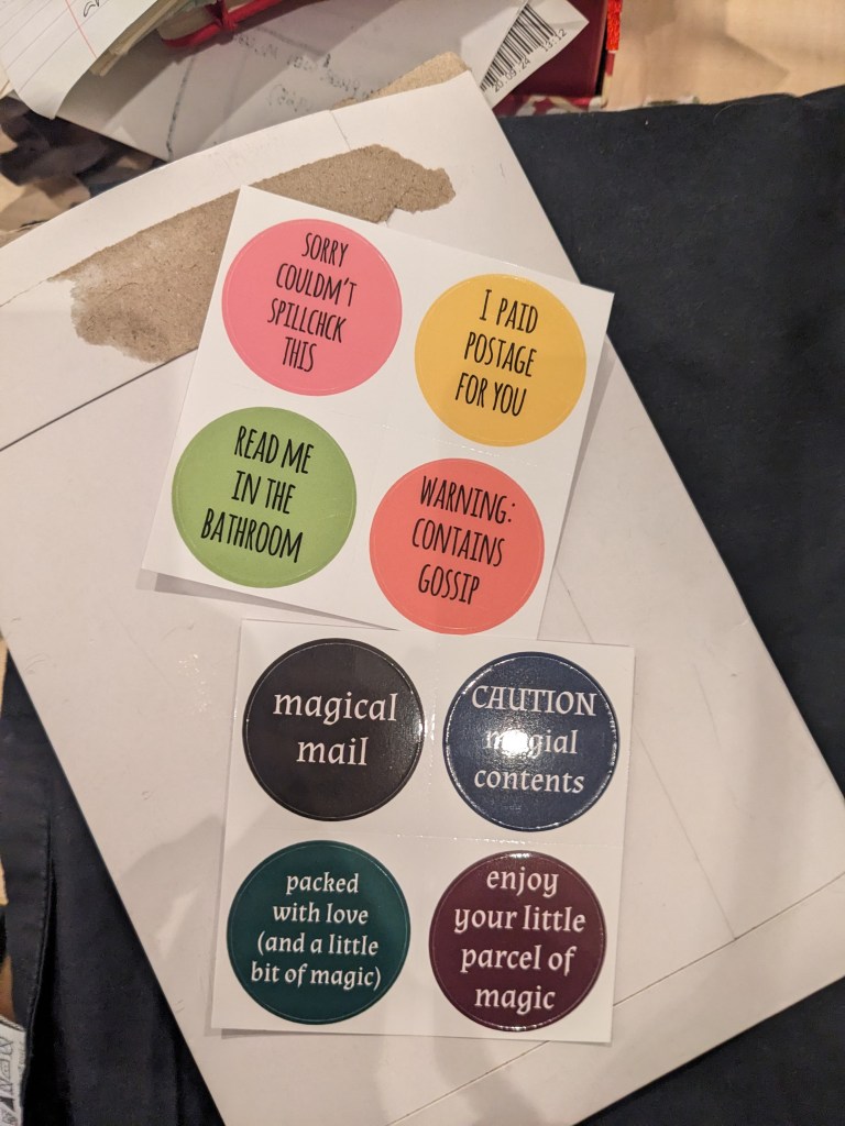 used card envelope and cotton cloth background with sheet of colourful stickers and sheet of witchy stickers